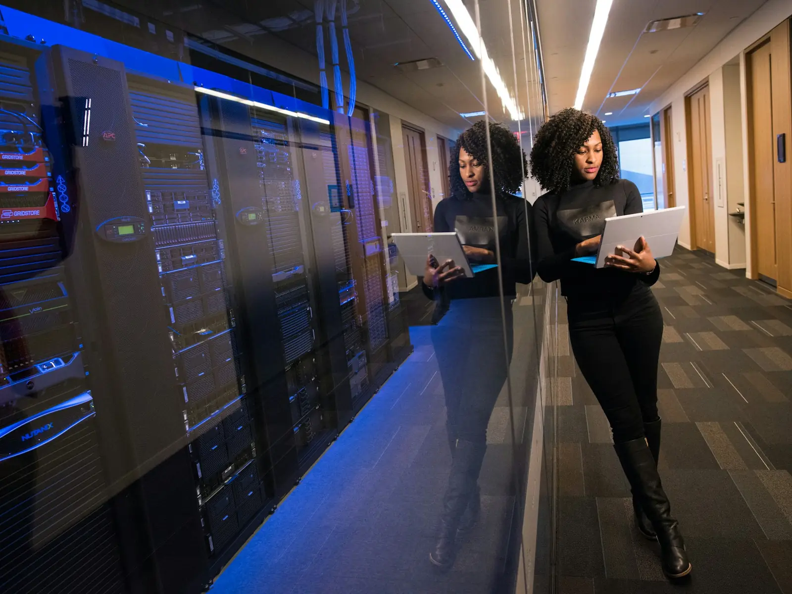 Two people with laptops reviewing work beside a wall of server racks