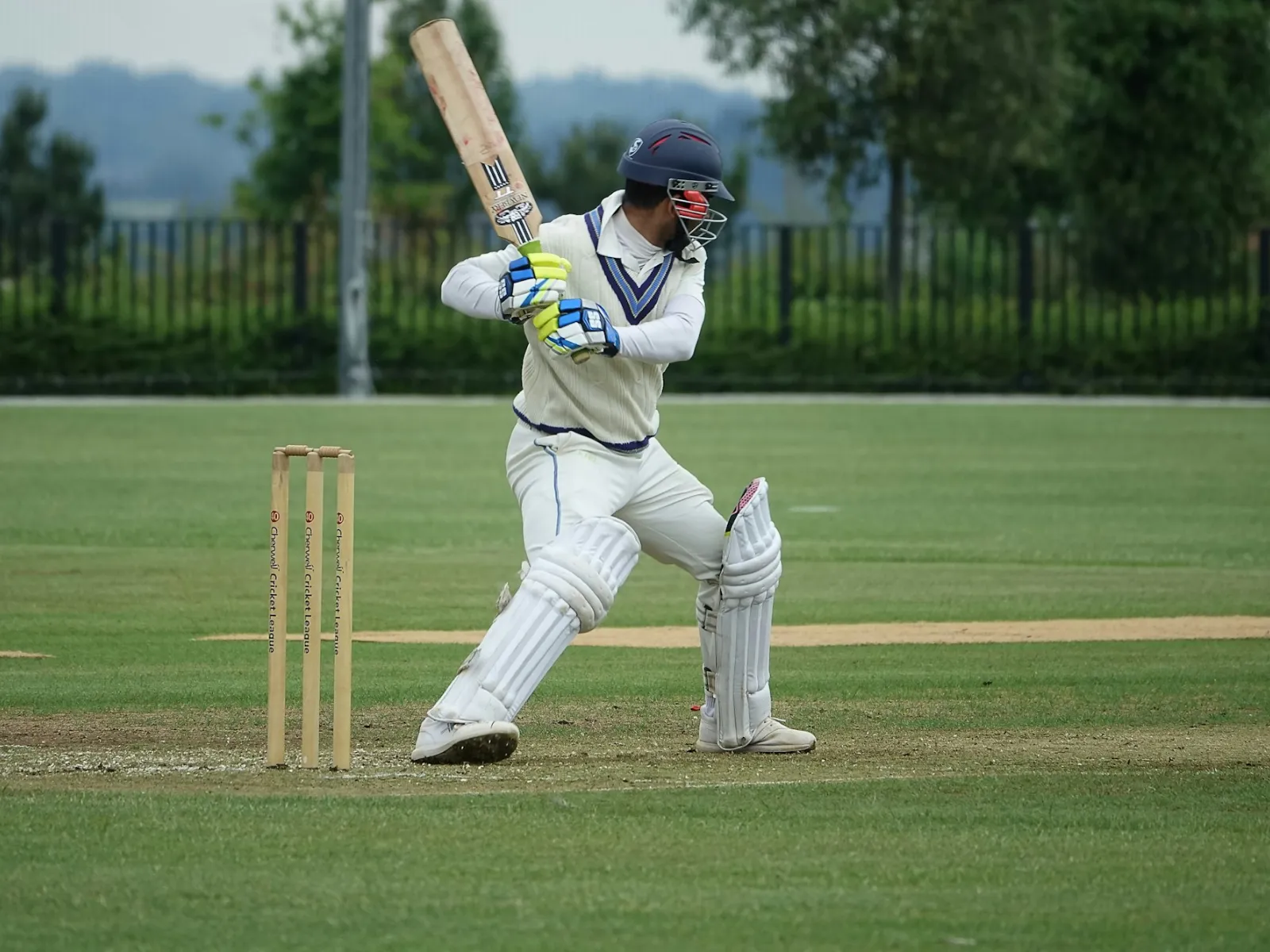 A batsman in whites and a helmet playing a shot beside the stumps